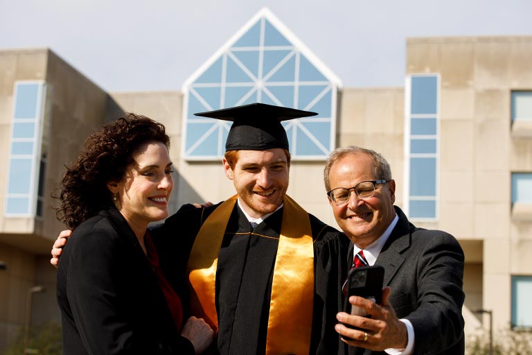 A student and his parents pose for a selfie with the IUPUI University Library behind them in the scene.