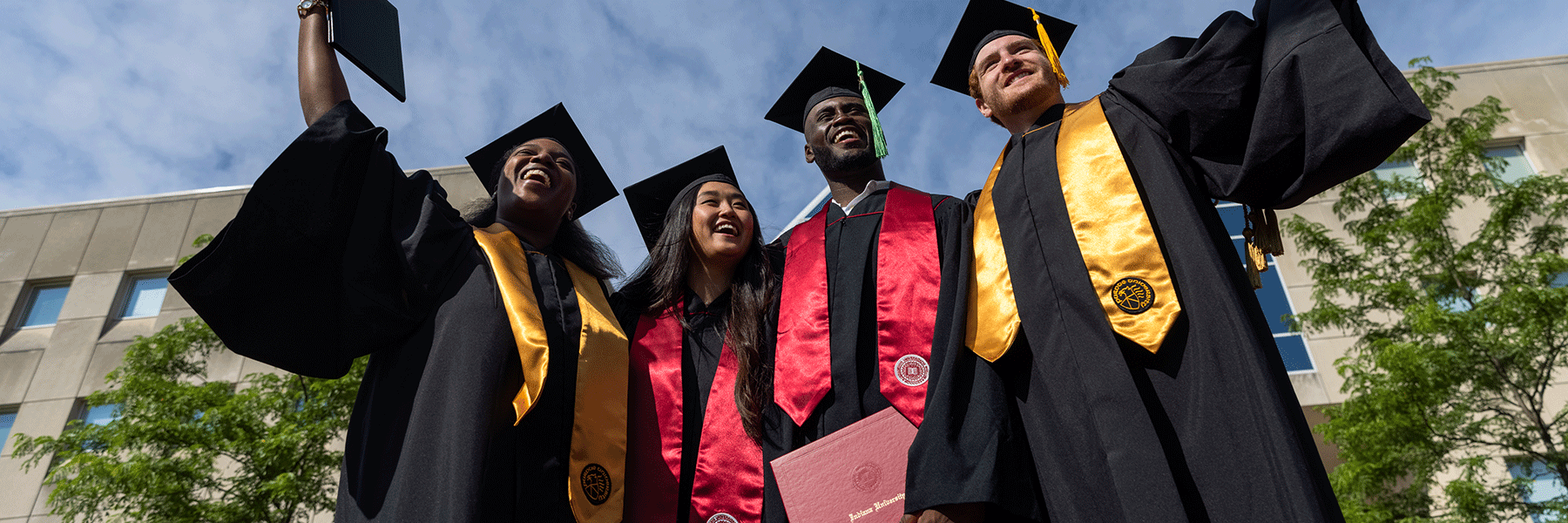 A group of graduates smile and pose in their commencement attire.