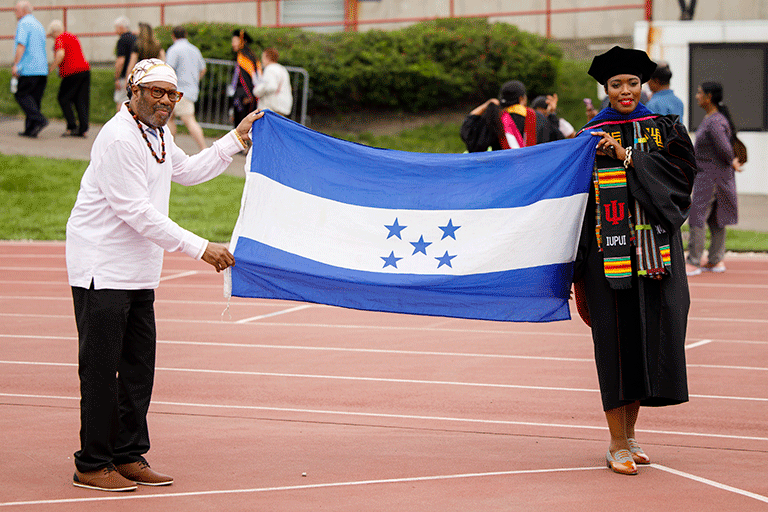 A man and a female graduate hold up the flag of Honduras between them after commencement.
