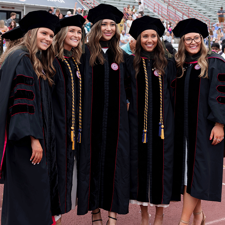 Five female graduates smile wearing their doctoral graduation robes.