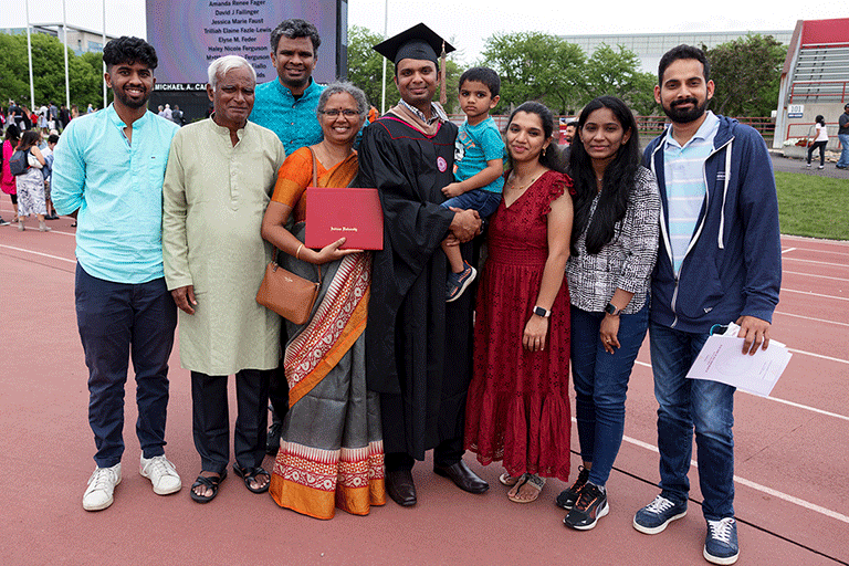 A family of nine pose for a picture with a male graduate holding a child in the middle.