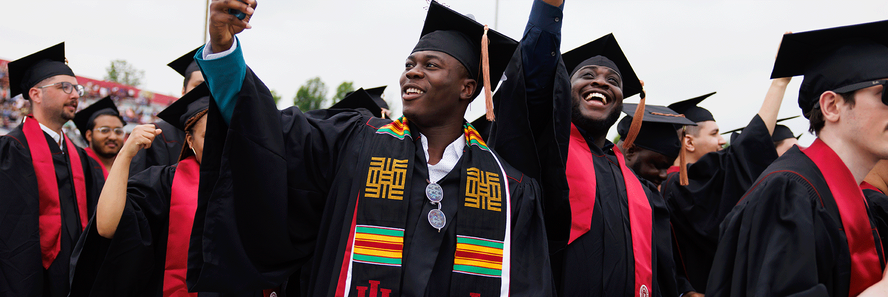 Two male graduates smile in a crowd during commencement.