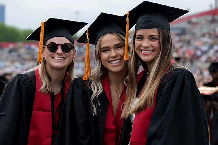 Three female graduates smile at the camera during the undergraduate ceremony