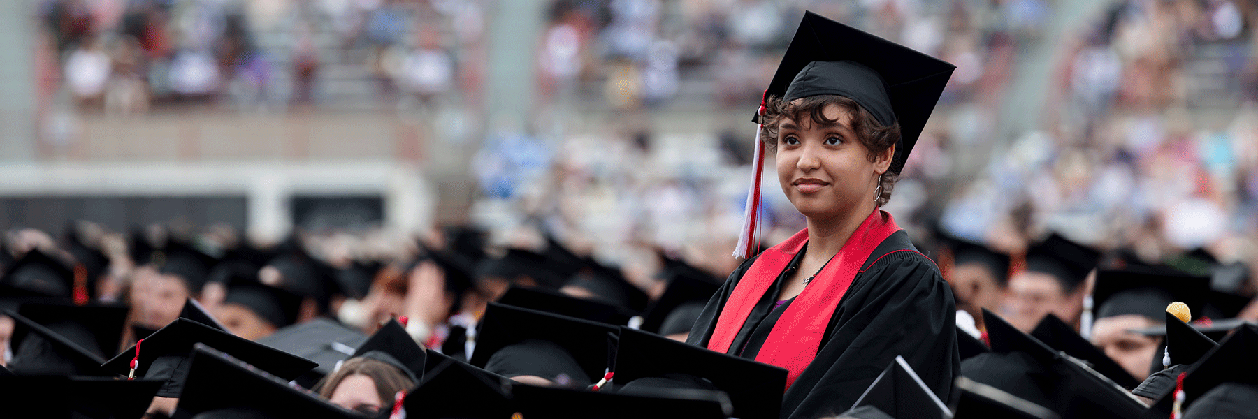 A female graduate standing in the crowd at commencement.