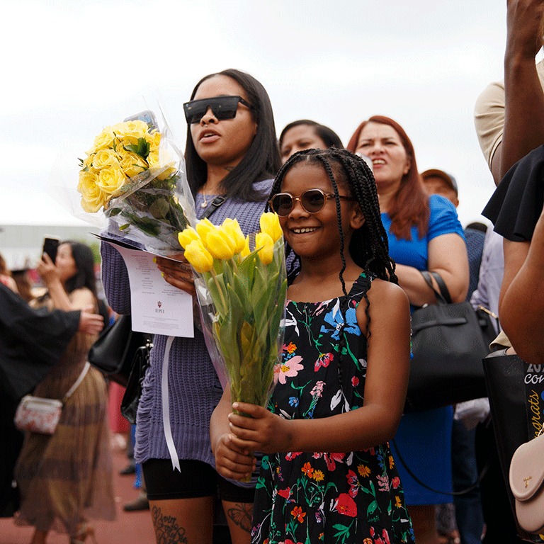 A little girl and a woman with sunglasses on both holding yellow flowers after the commencement ceremony.