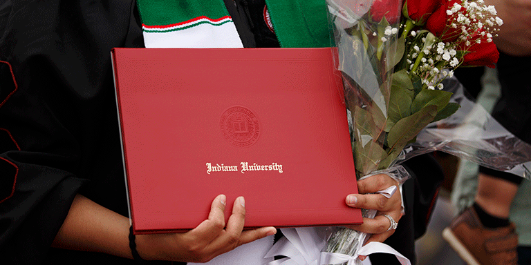 A closeup of an IU diploma cover and roses in a graduate's hands.