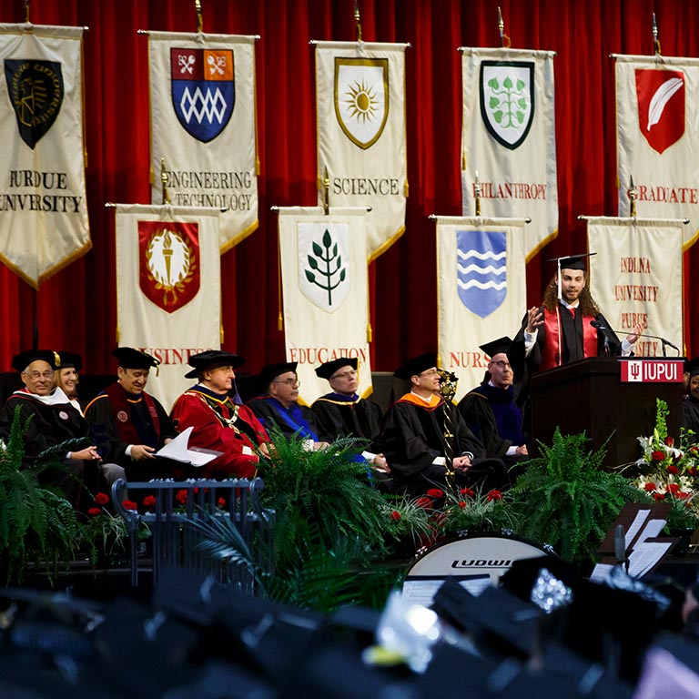 Cream colored banners bearing the graphic symbol and name of schools at IUPUI hang at the back of the Commencement stage