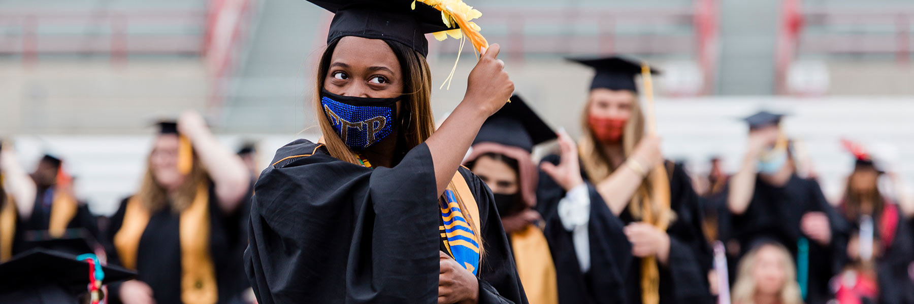 A female graduate stands to move her tassel from one side of her cap to the other