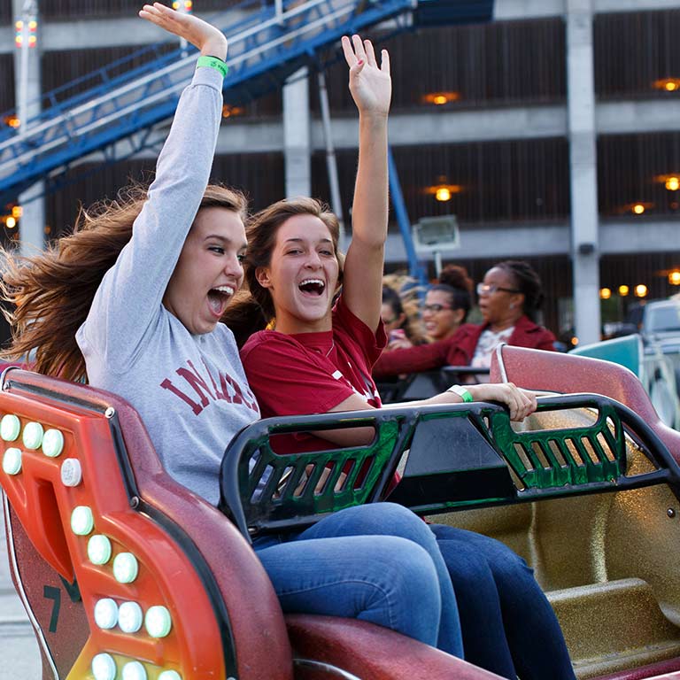 Two women riding in scrambler carnival ride with arms in the air and hair blowing in the wind