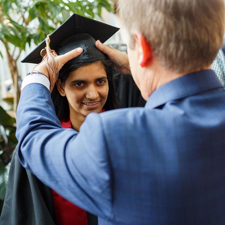 A man places a cap on a graduate at GradFair, testing for size