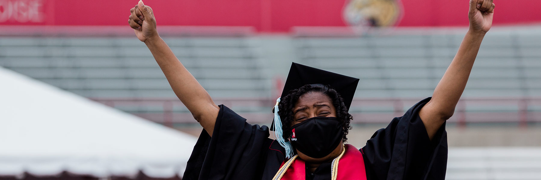 Master's graduate in cap and gown holds up her arms in excitement