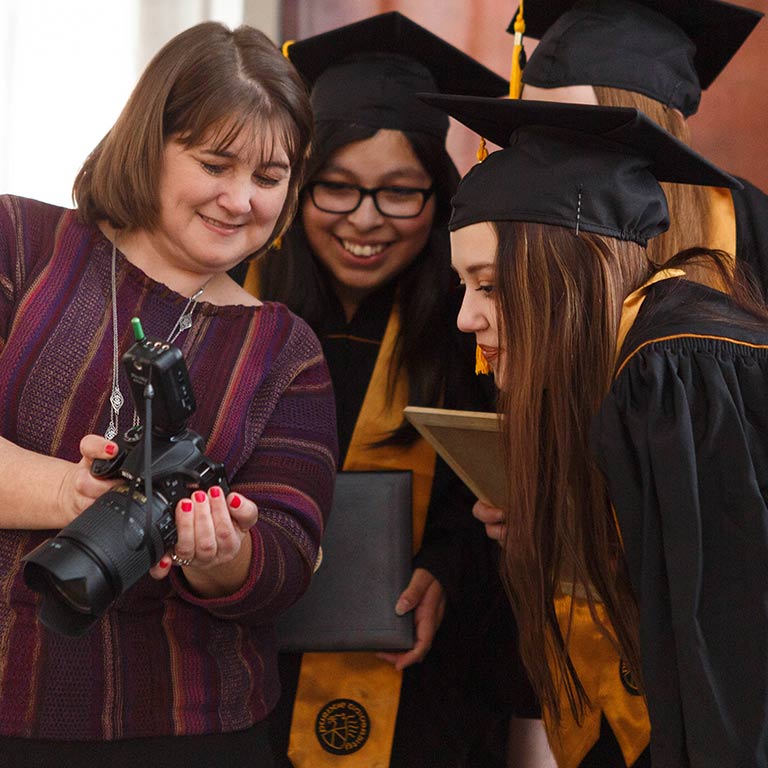 A photographer at GradFair shows three female students the screen on her camera so they can see the photo she took of them.