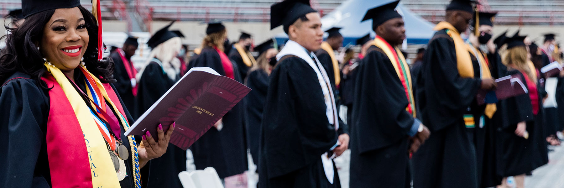 A graduate stands during the Commencement ceremony holding the official program