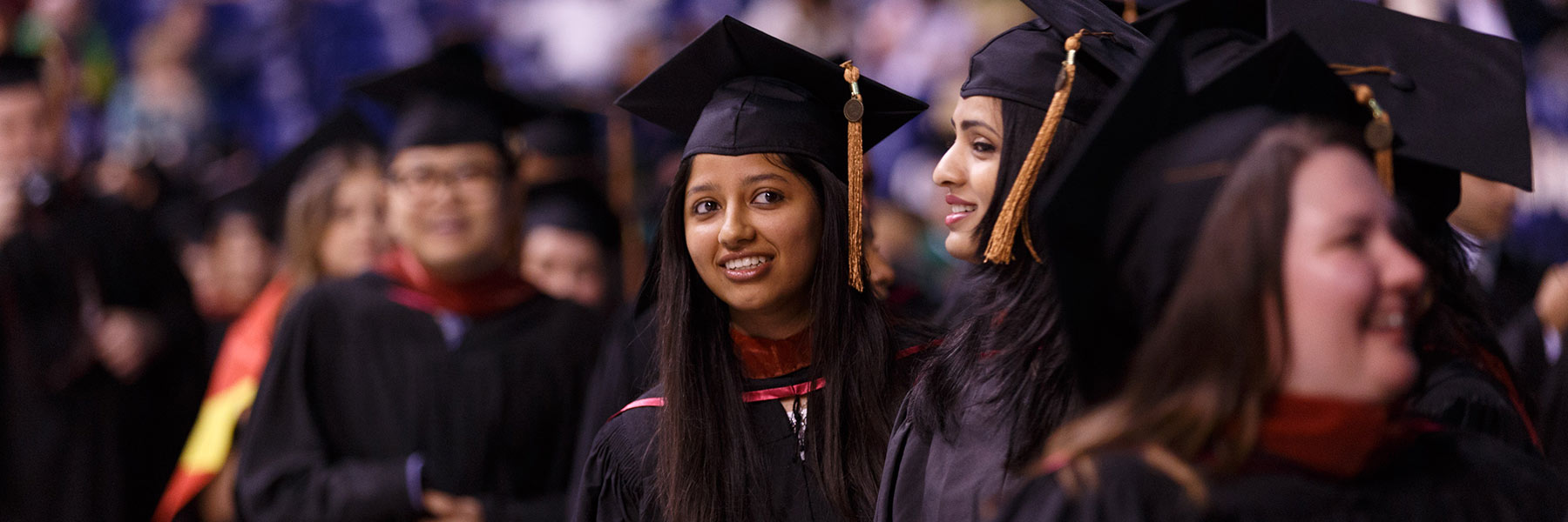 A line of graduates proceed in to the Commencement ceremony; one female leans out to look ahead