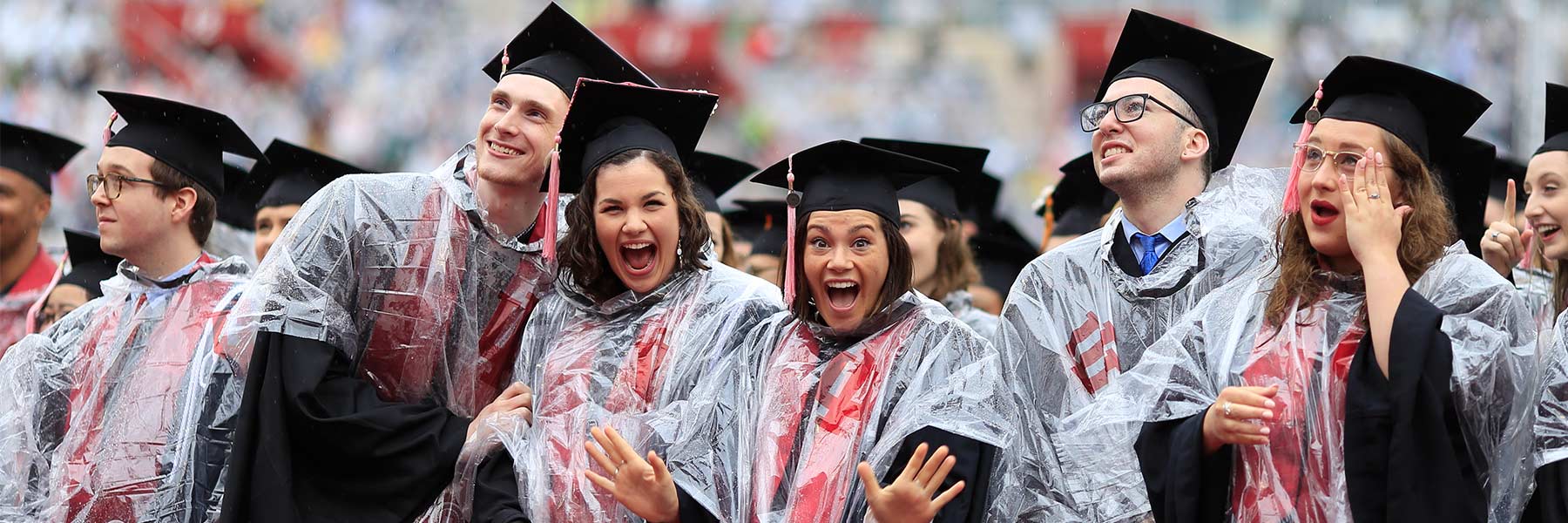 A group of graduates in caps, gowns and ponchos laugh while rain falls