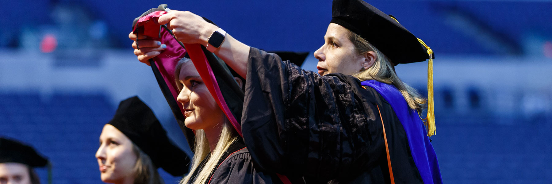 A faculty member places a doctoral hood over a student