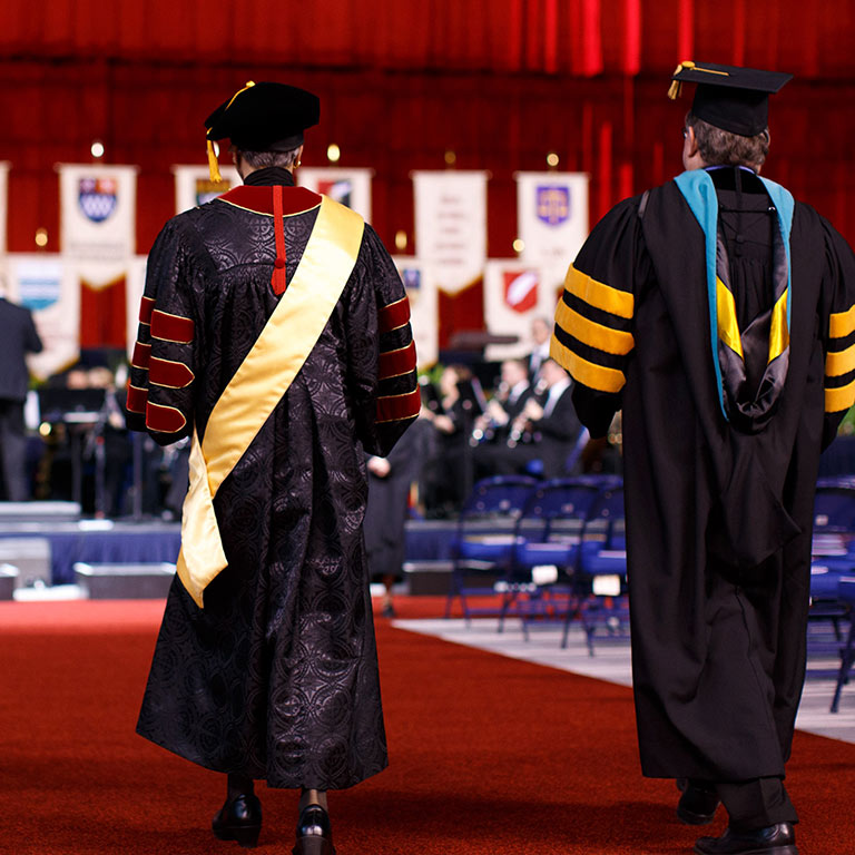 Two grand marshals walk down a red carpet toward the Commencement stage
