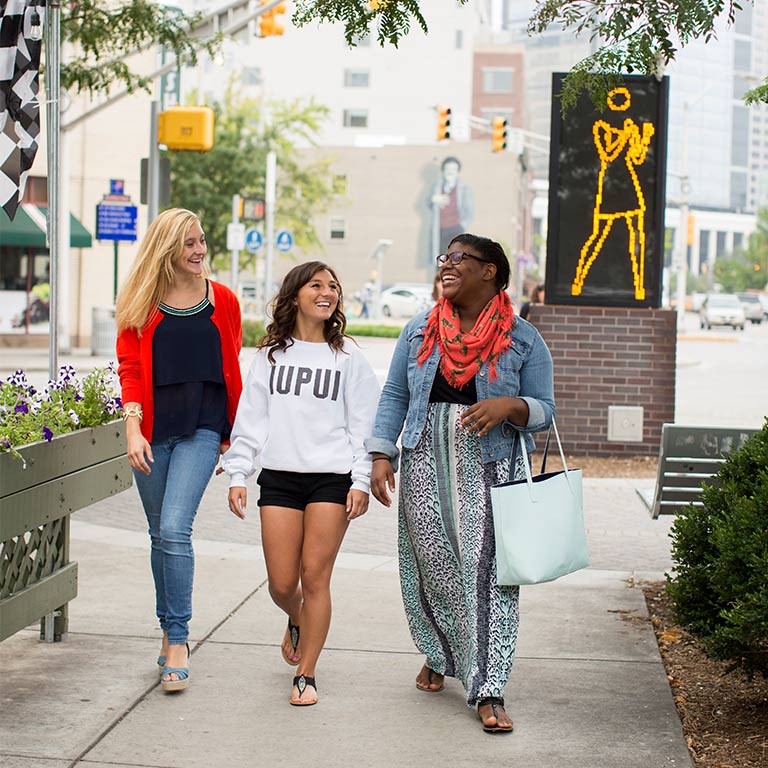 Three students walk on the sidewalk of Massachusetts Avenue, a downtown cultural district with restaurants seen further down the street