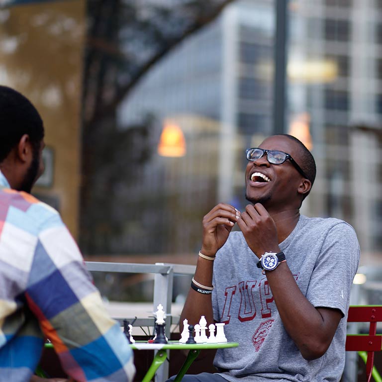 Two students sit at an outdoor chess game table in front of a business's window